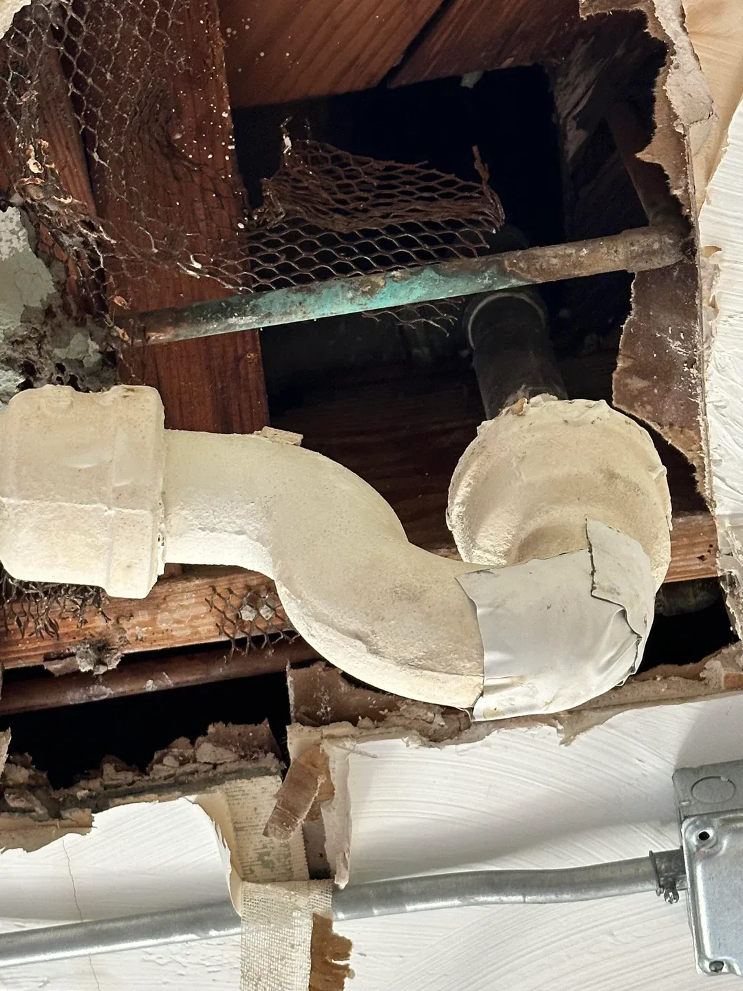 Opened ceiling showing a corroded pipe behind water-damaged drywall